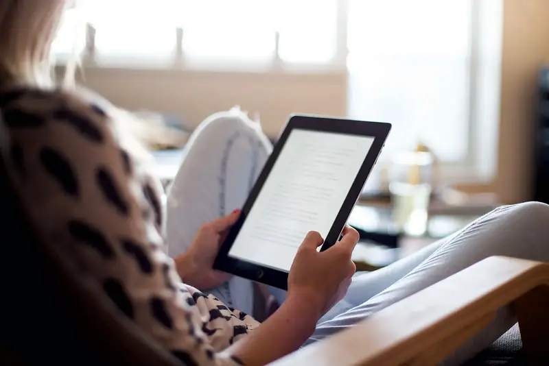 Une personne tient une tablette, installée dans un fauteuil près d’une fenêtre