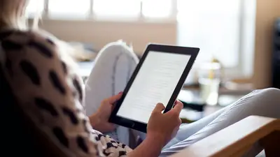 Une personne tient une tablette, installée dans un fauteuil près d’une fenêtre